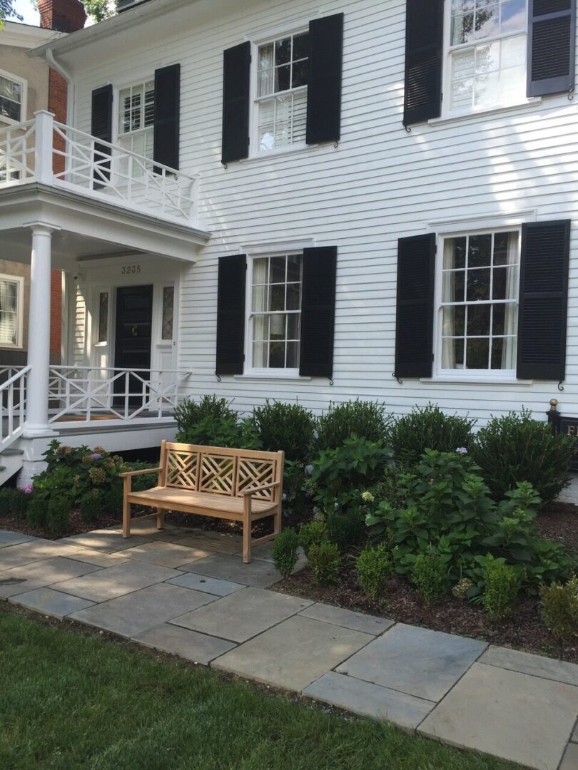 White house with black shutters and bench.