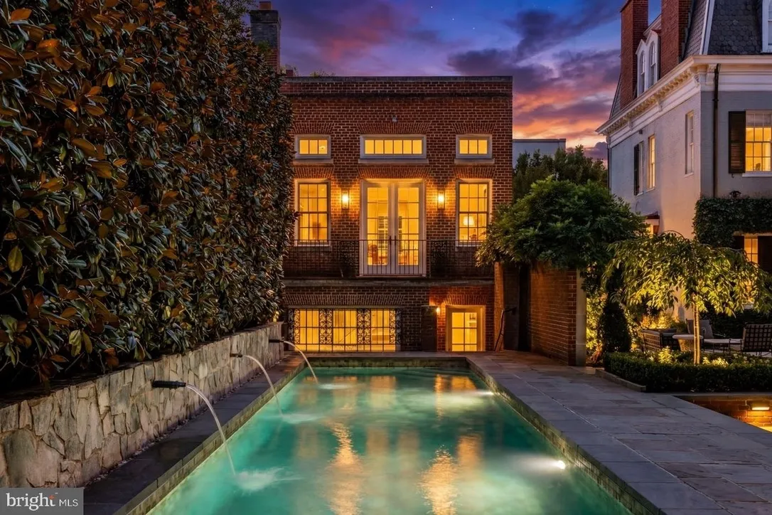 Elegant townhouse with illuminated pool at dusk.